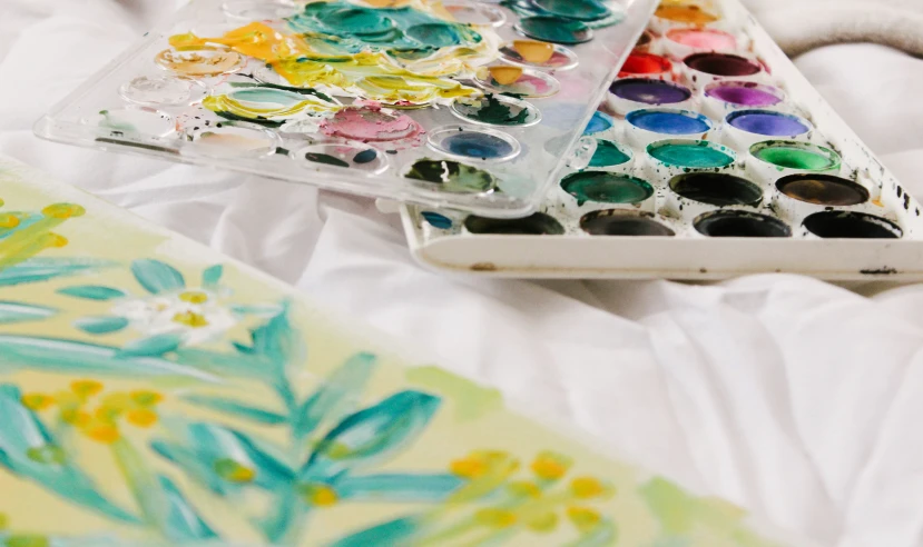 some colorful paints on a bed with white sheets