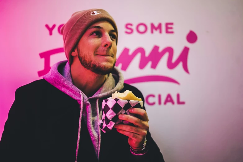 man eating a pastry in front of a pink wall