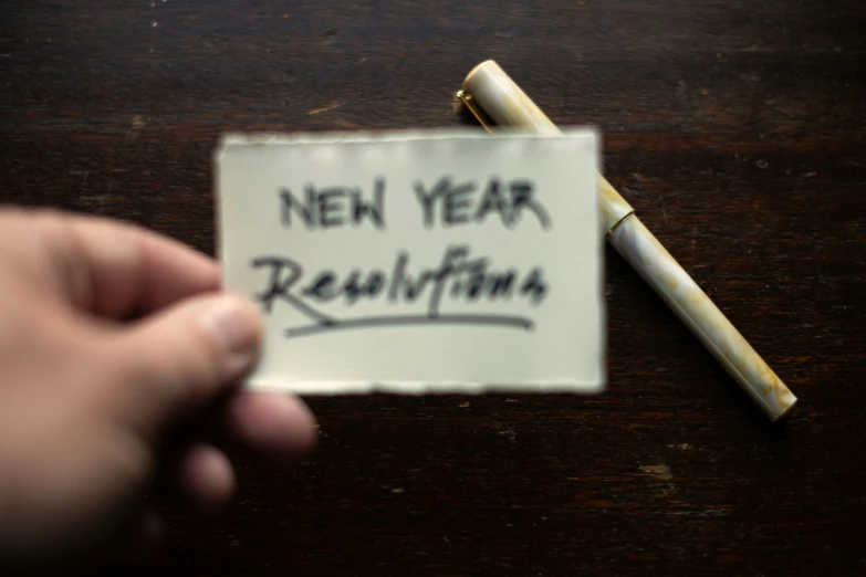 a piece of paper with a pen resting on it next to a note that says new year from rouhfina