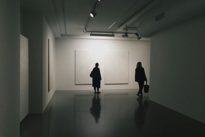 two people are walking inside a dark art gallery