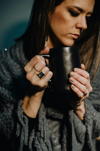 a woman holding a black cup and wearing rings