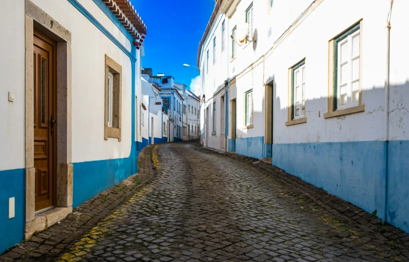 a narrow road with white buildings with blue trim