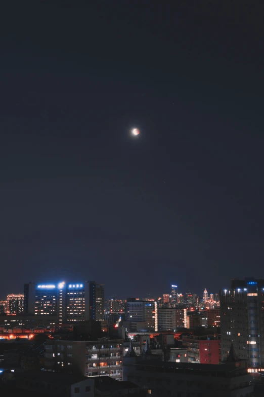 the moon is setting over a city with a distant object