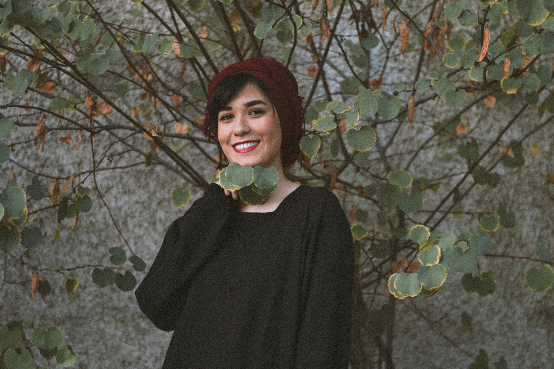 a woman poses by a tree with leaves