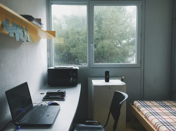 a bedroom with a window, a bed and a laptop computer on a desk