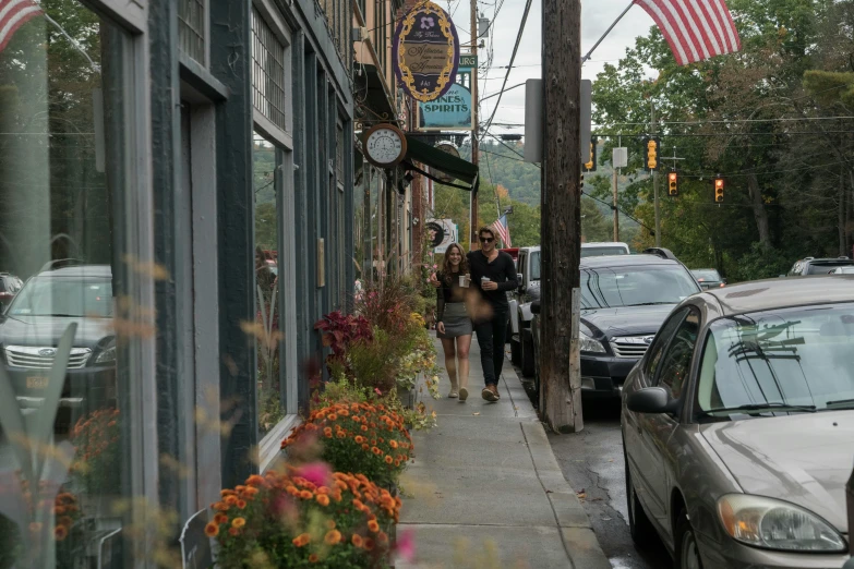 people are walking down a city sidewalk past the businesses