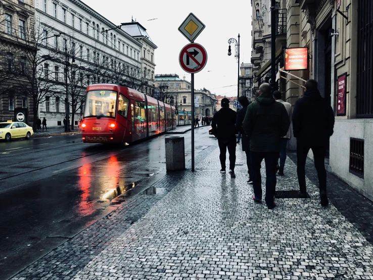 people walking on a sidewalk with a red and white train passing