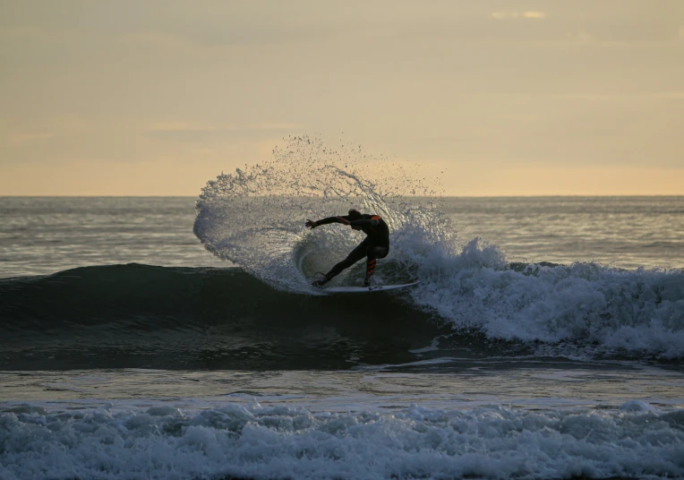 a surfer catching a wave at sunset with water splashing behind him