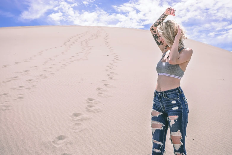 a woman in destroyed jeans standing on the beach and looking up at a foot print