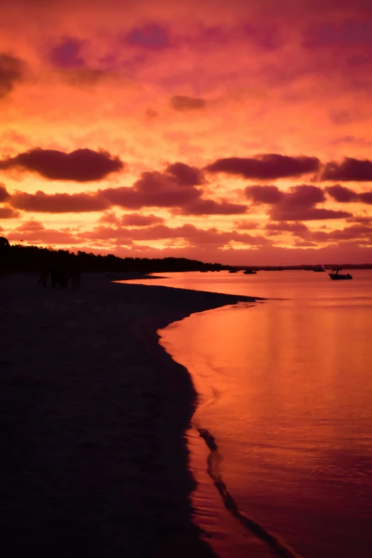 the sunset is on a beach and the two people are walking