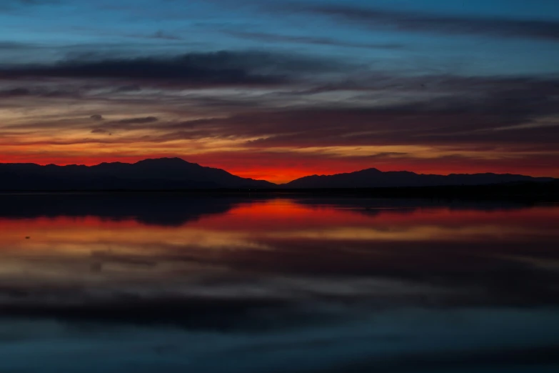 a beautiful sunset at a lake with mountains in the background