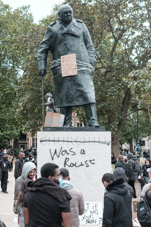 a statue of a man in a black coat is surrounded by people