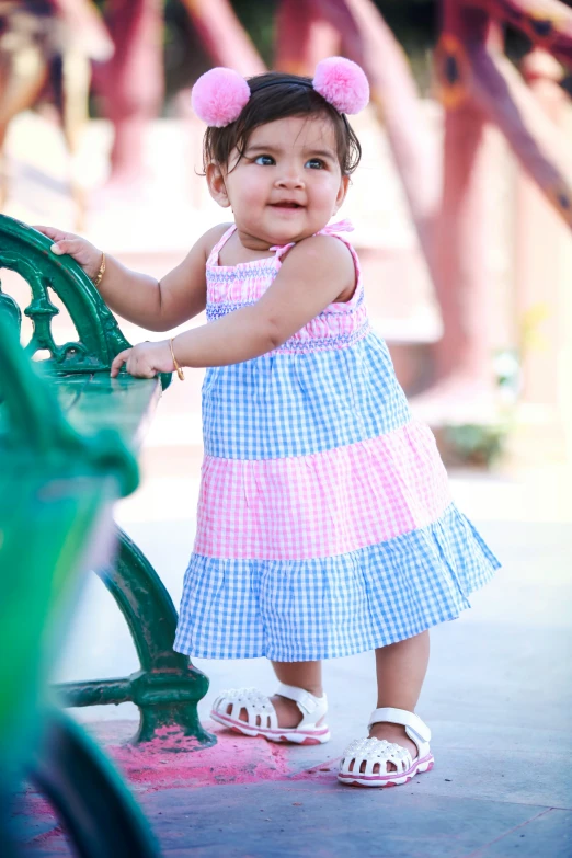 a small girl in a blue dress poses by a bench