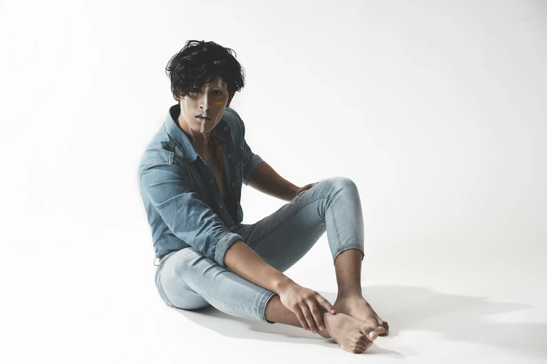 a man with dark hair and glasses sits on the floor in light blue jeans