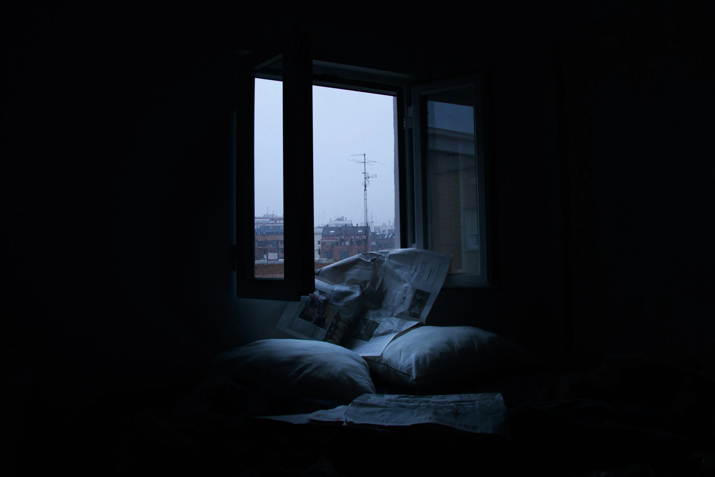 a window with pillows on the floor and a newspaper sitting on top of it