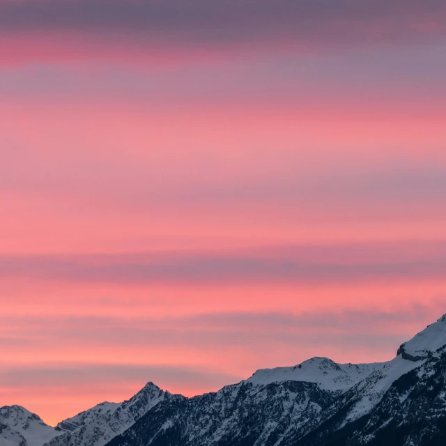 the view of some mountains and snow at sunset