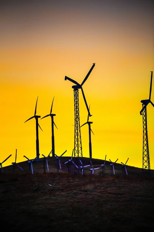 a group of wind turbines standing next to each other in front of a sunset