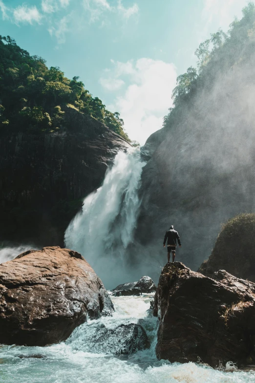 a man standing at the base of a waterfall near rocks