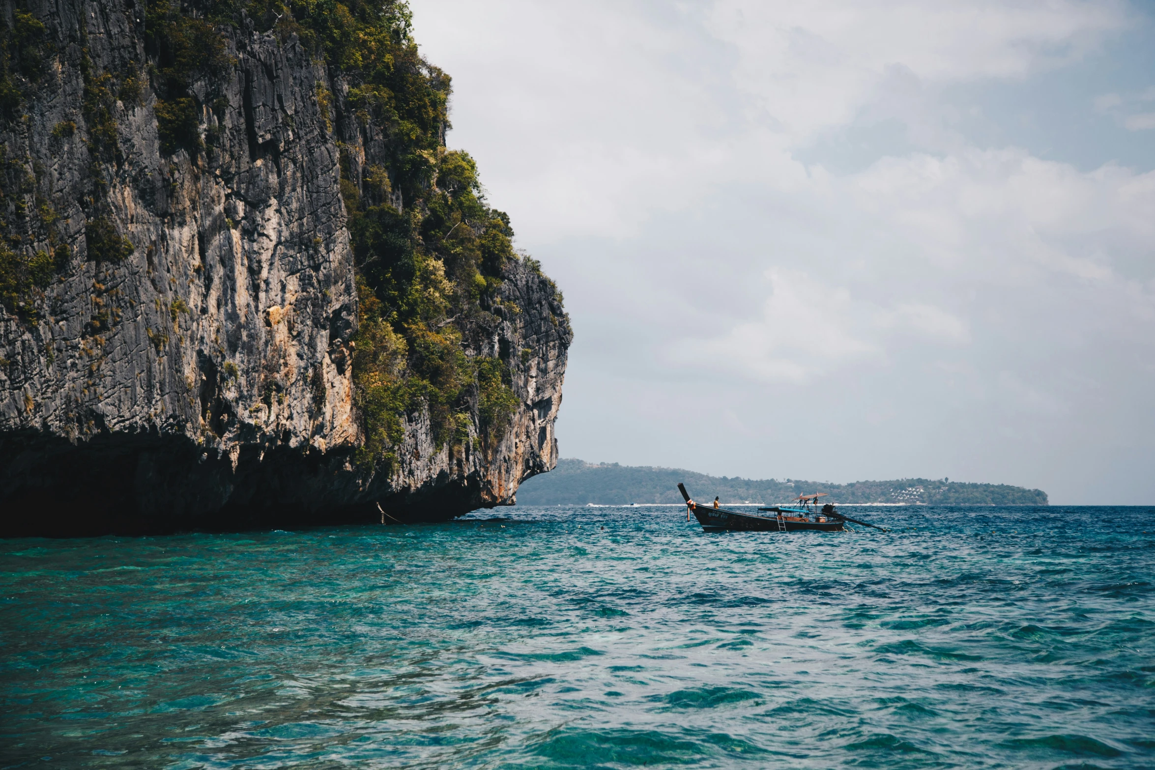 a boat floating past large cliffs with a mountain in the background