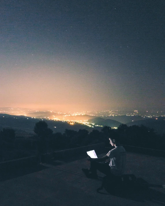a person sitting on top of a hill at night