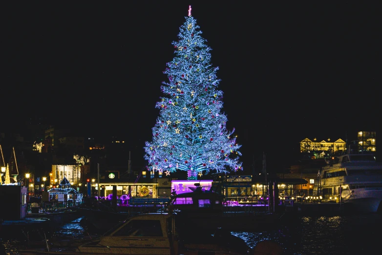 a very large lit christmas tree in front of a city