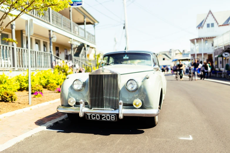 an old car sits in the middle of the street as people walk by