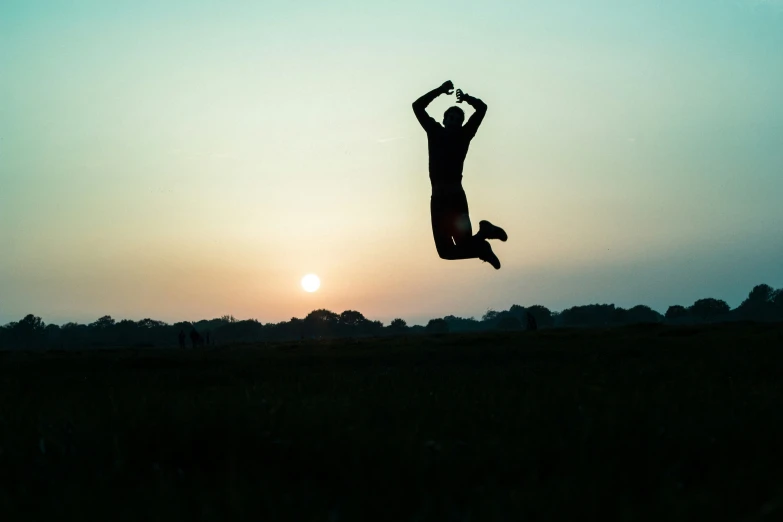 a man in mid air above the grass in front of a setting sun