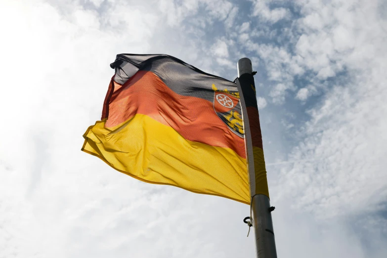 a yellow and red flag flying under a blue cloudy sky