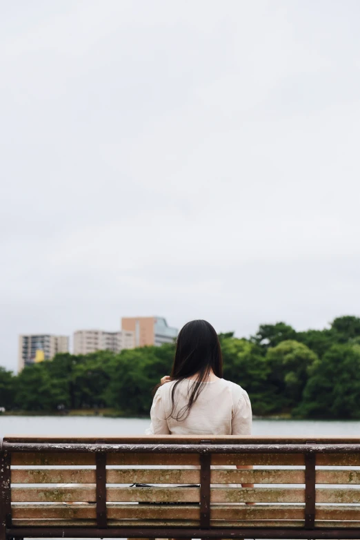 a woman sits on a bench in front of a river