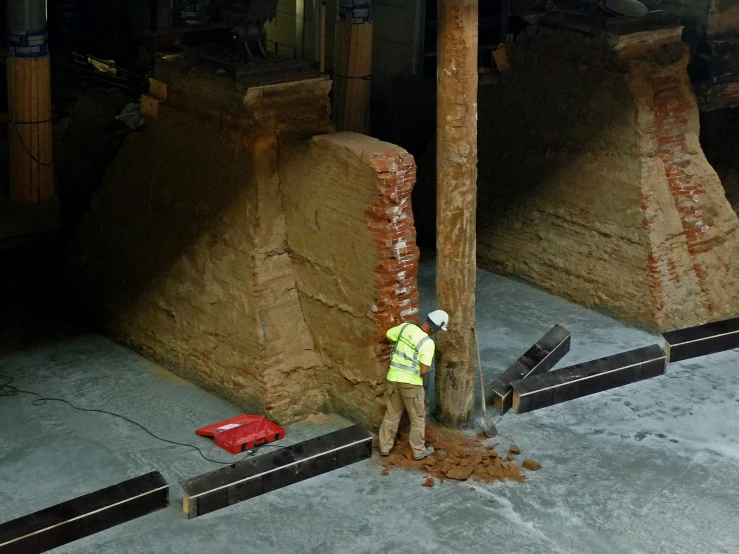 a worker with a green jacket and white helmet standing in front of a brick pillar