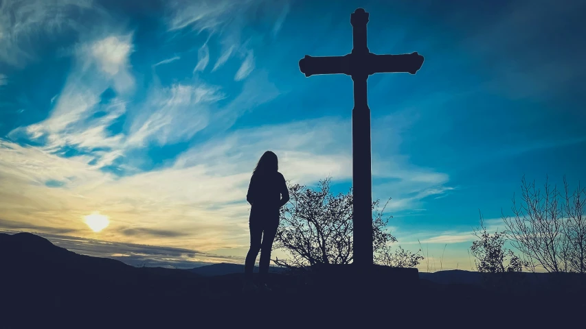 woman standing in front of a cross at sunset