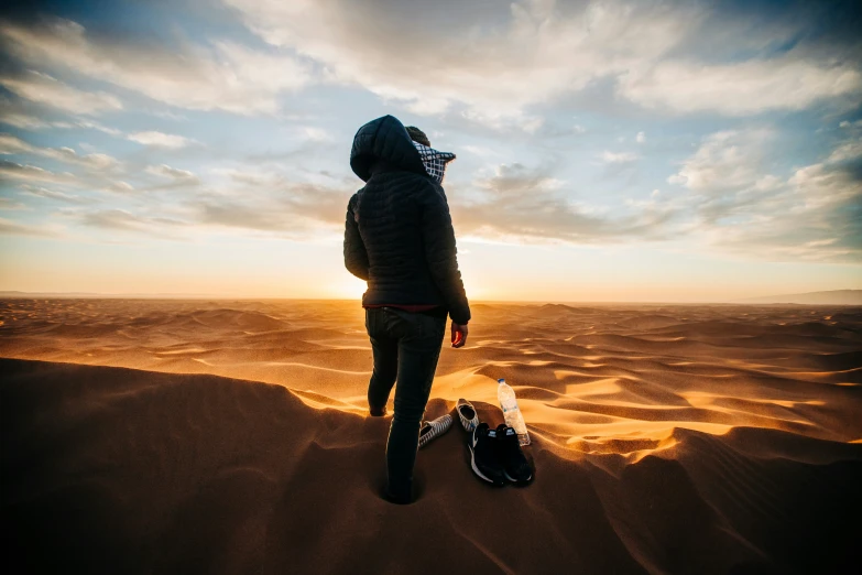 a person in a hooded jacket standing on sand with a bike