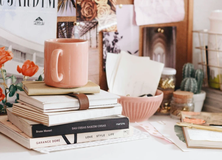 two books stacked on each other and one pink cup with the letter c on it