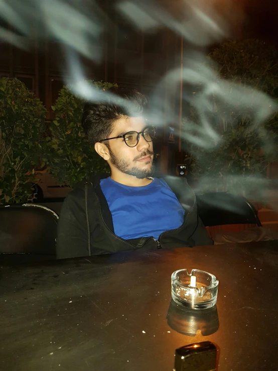 man sitting at table looking down and smoking a cigarette