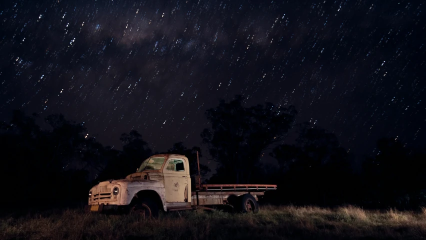 an old truck parked on a field with the lights turned on