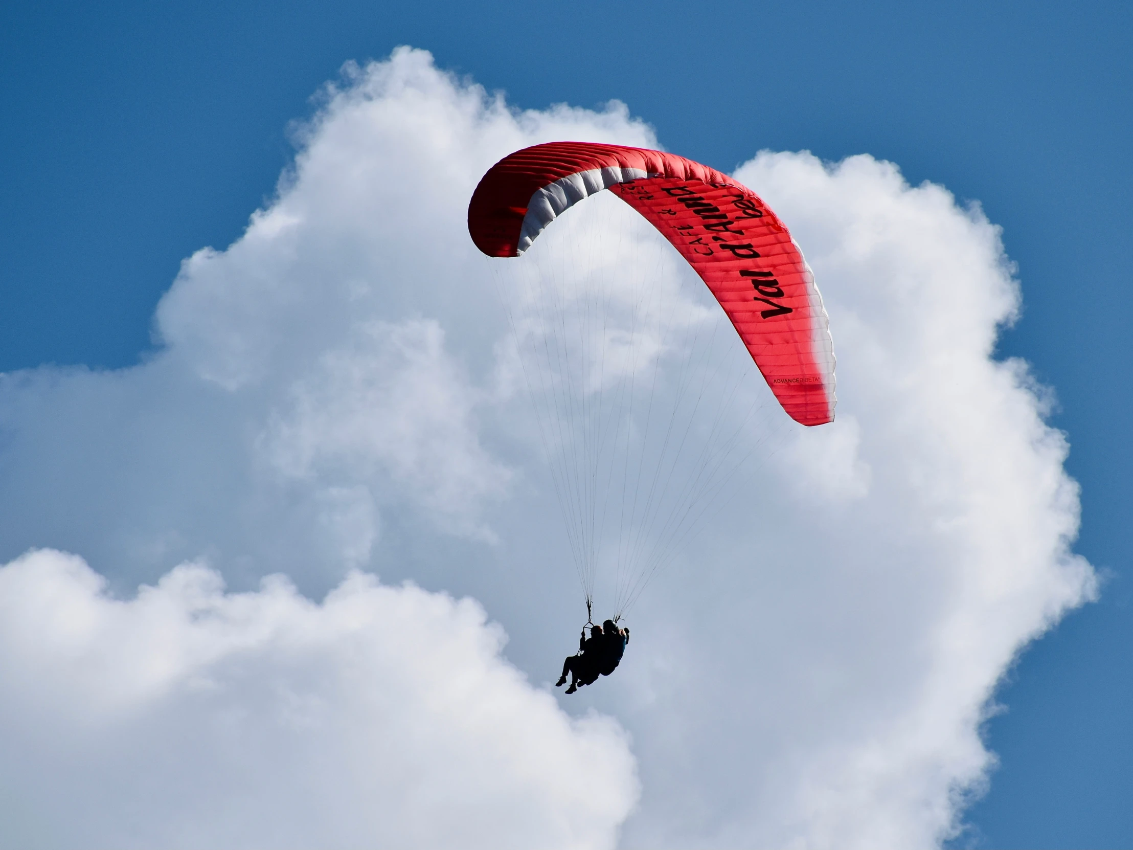 an orange parachute with black writing on the side and white clouds above