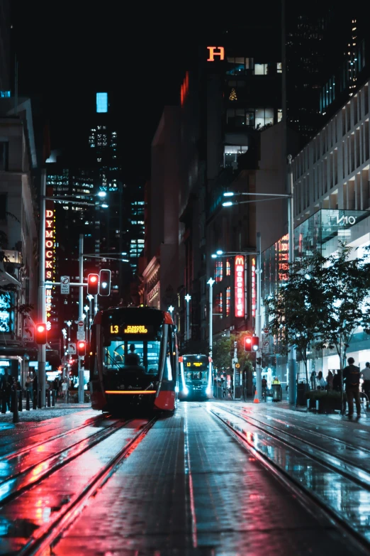 a city street is busy with a trolley on the rails at night