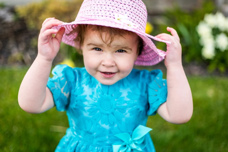 a  with a pink hat smiles while standing in the grass