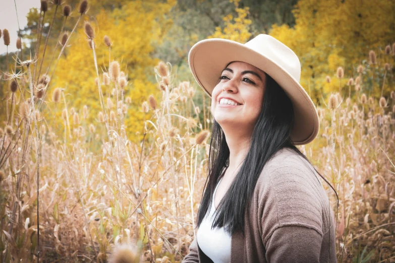 a woman standing in the tall grass with a hat on