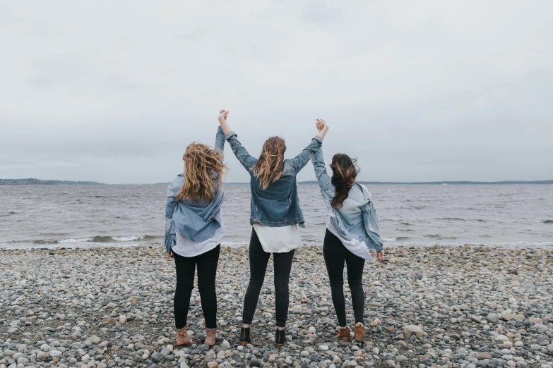 three women stand on the beach, arms in the air