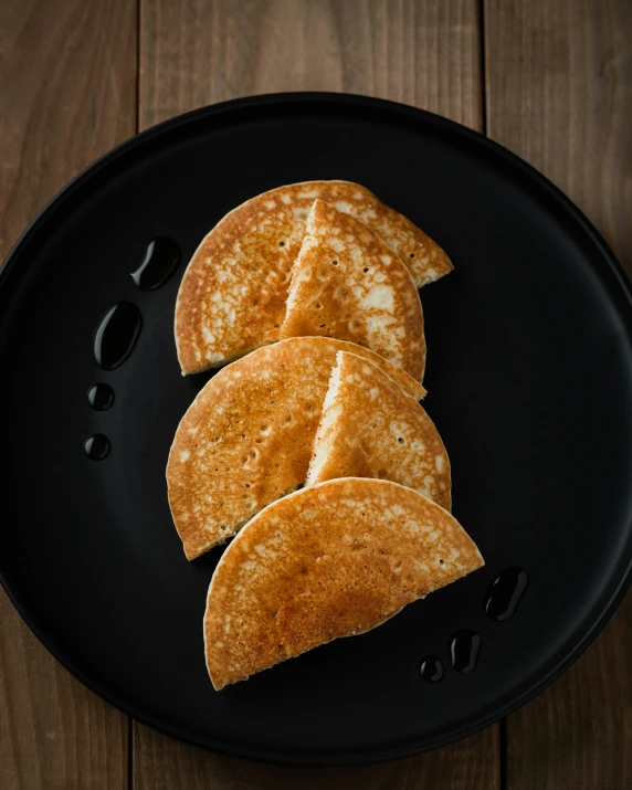 five pancakes on a black plate sitting on a wooden table