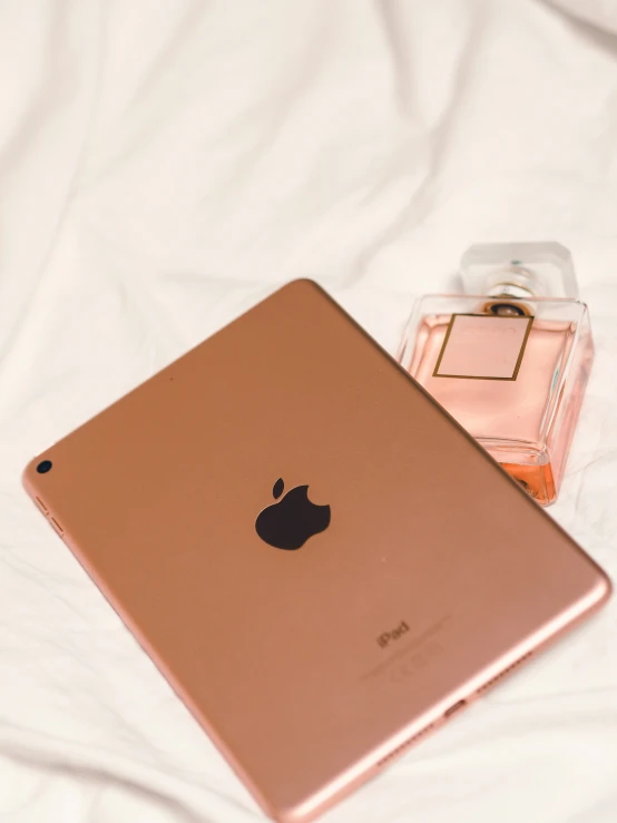 an apple ipad next to a perfume bottle on a bed