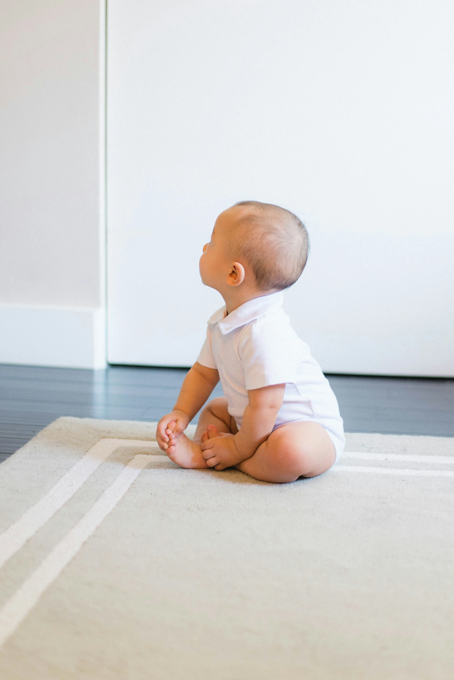 the small baby is sitting on the rug looking at soing