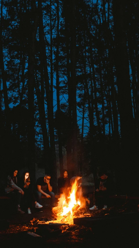 the people are sitting around the campfire at night