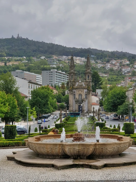 a fountain with water on the rocks in the center of a park in front of buildings