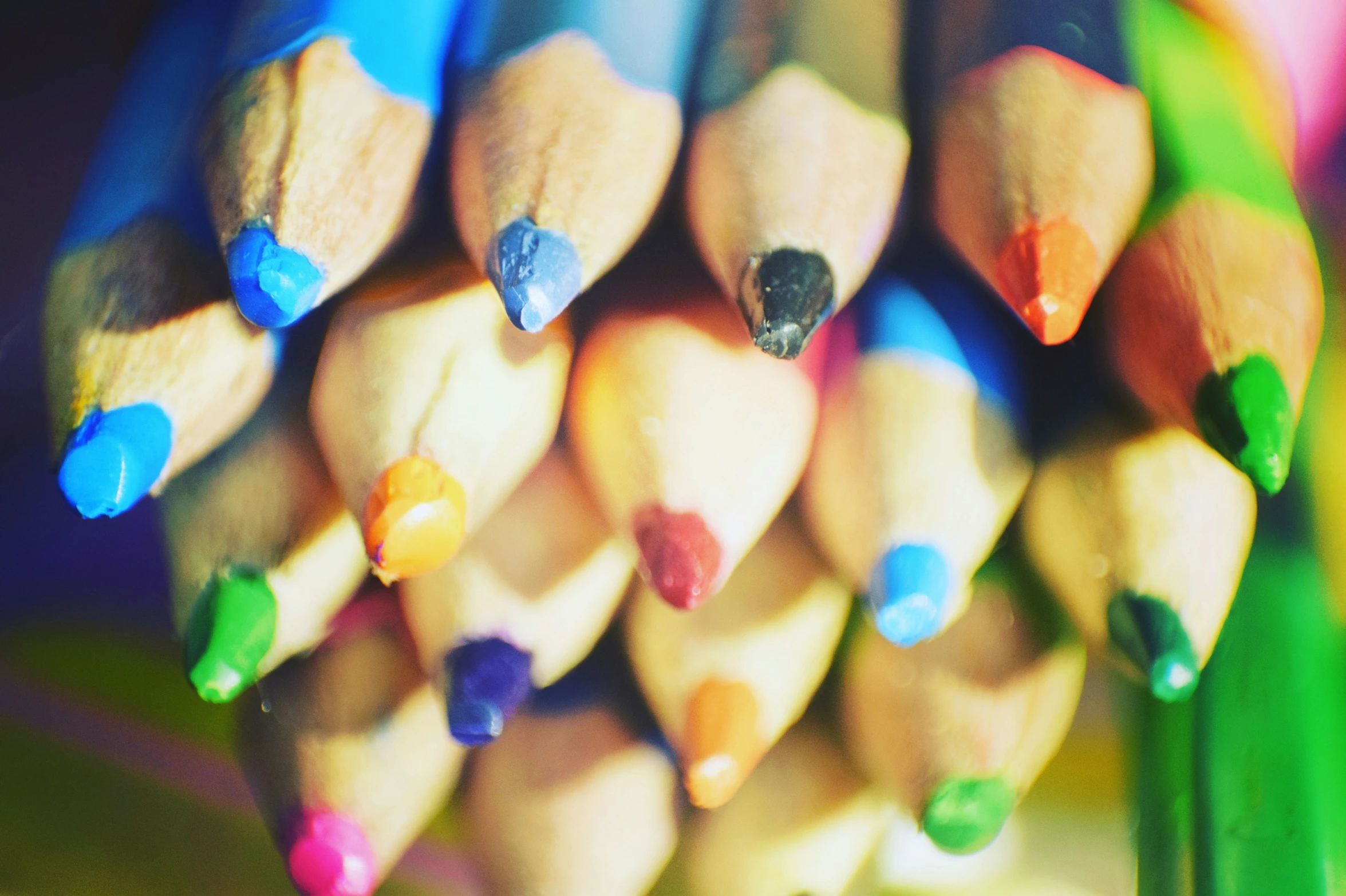 a group of colored pencils lined up with sharpener tips