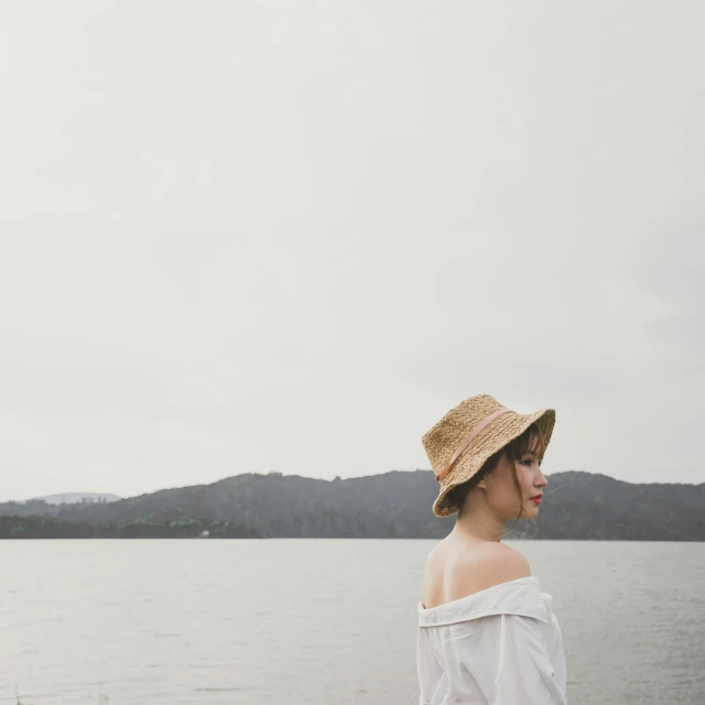 a woman standing near the water with her hat on