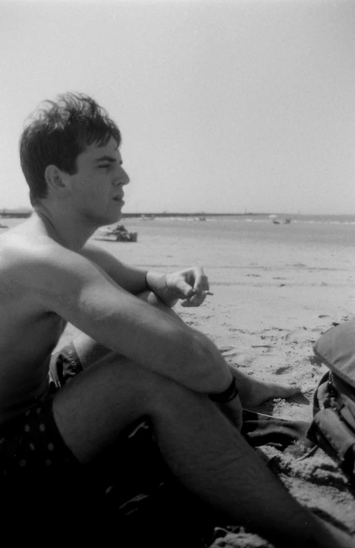 a young man sits on a blanket on the beach
