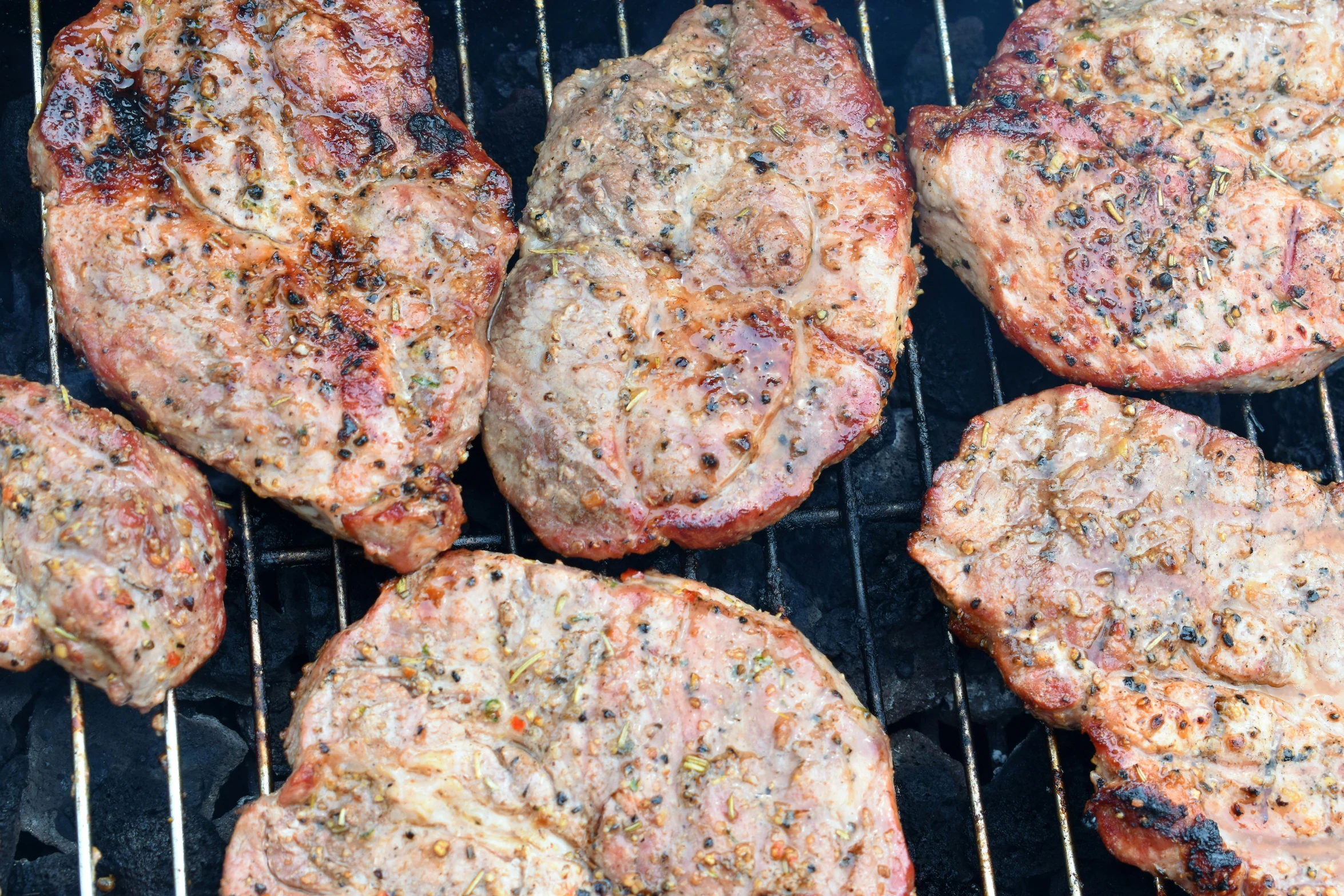 four hamburger patties cooking on an outdoor grill