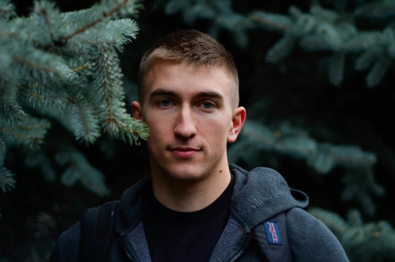 the man wearing a backpack is standing in front of evergreen trees